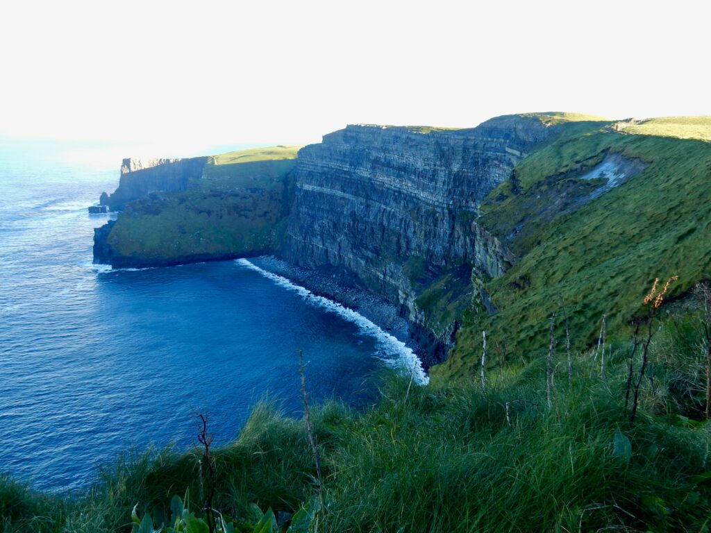 Aerial view of a scenic coastline with lush green cliffs and crystal-clear blue ocean waters.